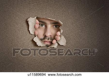 Picture - Portrait of a mid adult Caucasian man peeking from ripped paper hole. Fotosearch