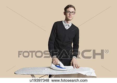 Stock Photo - Portrait of a mid adult man looking away while ironing over colored background. Fotosearch