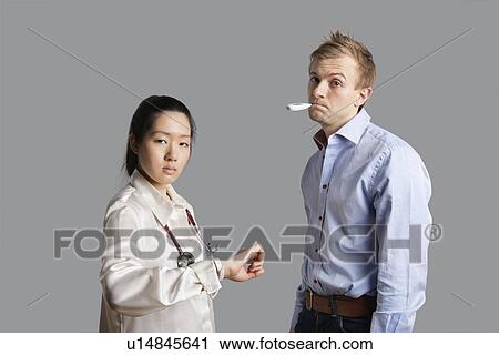 Stock Image - Portrait of a patient with thermometer in mouth standing with doctor. Fotosearch