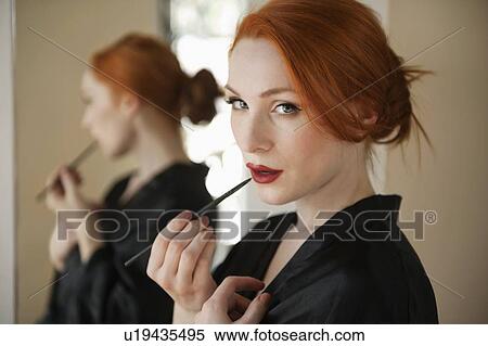 Stock Photography - Portrait of a redheaded woman applying lip liner. Fotosearch