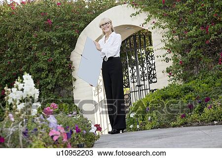 Portrait of a senior female real estate agent holding sign board in front of entrance gate View Large Photo Image Stock Image - Portrait of a senior female real estate agent holding sign board in front of entrance gate. Fotosearch