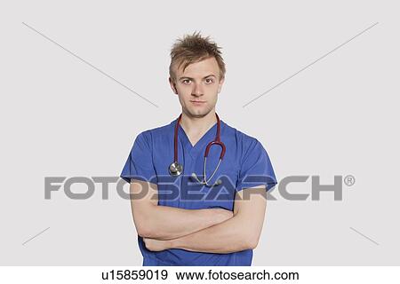 Stock Photo - Portrait of a serious male surgeon standing with arms crossed over gray background. Fotosearch