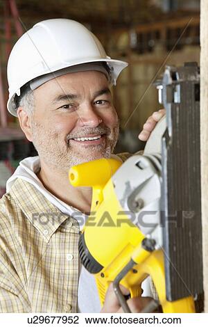 Stock Image - Portrait of a smiling male construction worker cutting wood with a circular saw. Fotosearch
