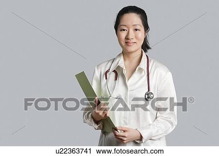 Portrait of a young Asian female doctor with a clipboard over gray background View Large Photo Image Stock Image - Portrait of a young Asian female doctor with a clipboard over gray background. Fotosearch