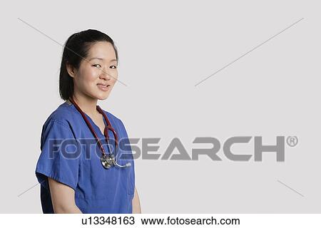 Stock Image - Portrait of a young Asian female surgeon smiling over gray background. Fotosearch