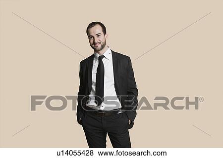 Stock Photo - Portrait of a young businessman with hands in pockets over colored background. Fotosearch