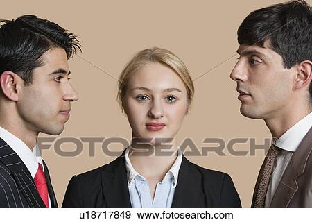Stock Photo - Portrait of a young businesswoman with male colleagues staring at each other over colored background. Fotosearch