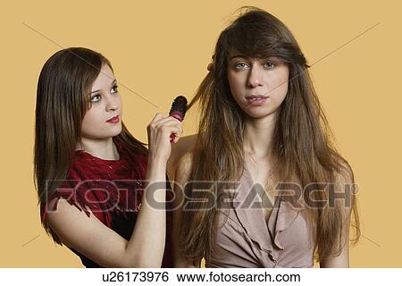 Stock Photograph - Portrait of a young female model getting her hair styled over colored background. Fotosearch