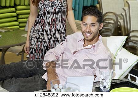 Portrait of a young man lying on sofa while woman standing in background View Large Photo Image Stock Image - Portrait of a young man lying on sofa while woman standing in background. Fotosearch