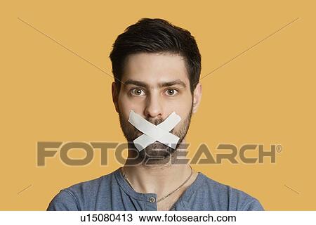 Portrait of a young man with tape on mouth over colored background View Large Photo Image Stock Image - Portrait of a young man with tape on mouth over colored background. Fotosearch