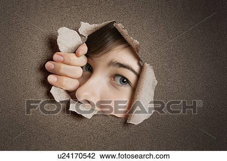 Stock Image - Portrait of a young Middle eastern woman peeking from ripped white paper hole. Fotosearch