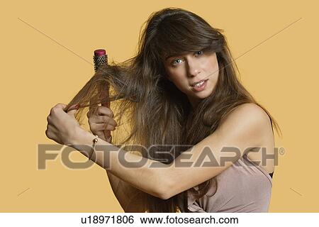 Stock Photograph - Portrait of a young woman brushing hair over colored background. Fotosearch