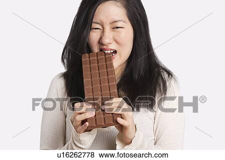 Portrait of a young woman eating a large chocolate bar over light gray background View Large Photo Image Stock Photo - Portrait of a young woman eating a large chocolate bar over light gray background. Fotosearch
