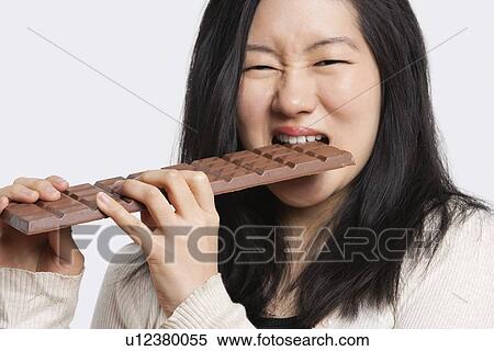 Portrait of a young woman eating a large chocolate bar over light gray background View Large Photo Image Stock Photography - Portrait of a young woman eating a large chocolate bar over light gray background. Fotosearch