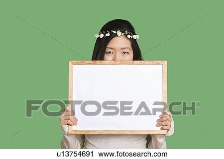 Portrait of a young woman hiding her face with a blank whiteboard over green background View Large Photo Image Stock Image - Portrait of a young woman hiding her face with a blank whiteboard over green background. Fotosearch
