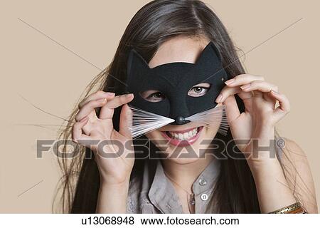 Portrait of a young woman imitating as cat while looking through eye mask over colored background View Large Photo Image Stock Photo - Portrait of a young woman imitating as cat while looking through eye mask over colored background. Fotosearch