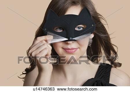 Portrait of a young woman looking through eye mask over colored background View Large Photo Image Stock Image - Portrait of a young woman looking through eye mask over colored background. Fotosearch