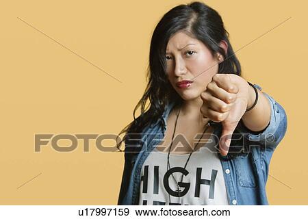 Stock Photo - Portrait of a young woman showing thumbs down over colored background. Fotosearch