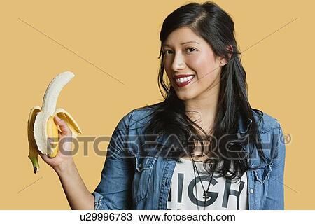 Stock Image - Portrait of a young woman with banana over colored background. Fotosearch