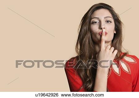 Stock Photograph - Portrait of a young woman with finger on lips over colored background. Fotosearch