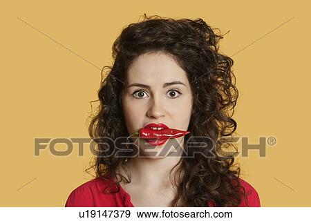 Portrait of a young woman with red chili pepper in mouth over colored background View Large Photo Image Stock Photo - Portrait of a young woman with red chili pepper in mouth over colored background. Fotosearch