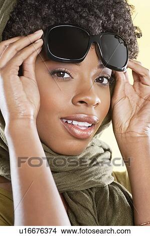 Portrait of an African American woman holding sunglasses with a stole round her neck over colored background View Large Photo Image Picture - Portrait of an African American woman holding sunglasses with a stole round her neck over colored background. Fotosearch