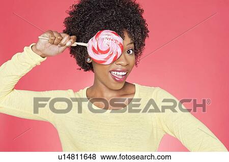 Portrait of an African American woman holding candy over her eye against colored background View Large Photo Image Stock Photo - Portrait of an African American woman holding candy over her eye against colored background. Fotosearch