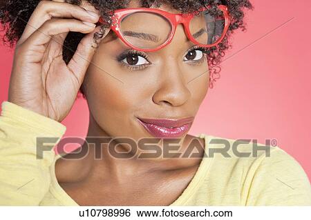 Stock Photograph - Portrait of an African American woman holding retro glasses over colored background. Fotosearch