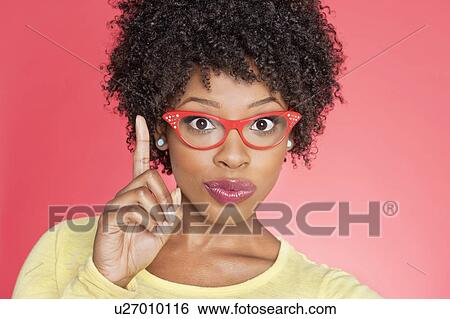 Portrait of an African American woman in retro glasses pointing upward over colored background View Large Photo Image Stock Photograph - Portrait of an African American woman in retro glasses pointing upward over colored background. Fotosearch