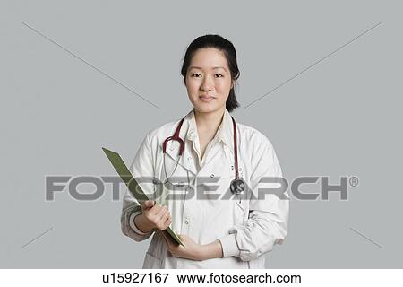 Stock Photo - Portrait of an Asian female doctor holding a clipboard over gray background. Fotosearch