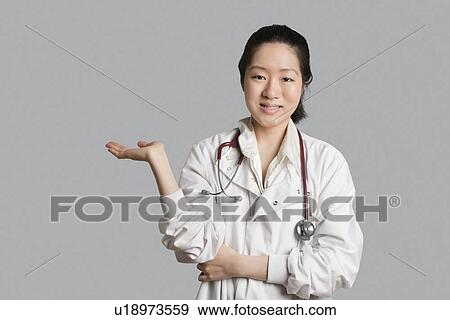 Portrait of an Asian female doctor displaying an invisible product over gray background View Large Photo Image Stock Photo - Portrait of an Asian female doctor displaying an invisible product over gray background. Fotosearch