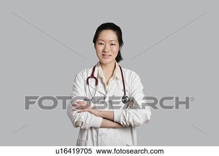 Stock Photography - Portrait of an Asian female doctor standing with arms crossed over gray background. Fotosearch
