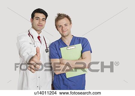 Portrait of an Indian doctor gesturing thumbs up while standing with male nurse over light gray background View Large Photo Image Picture - Portrait of an Indian doctor gesturing thumbs up while standing with male nurse over light gray background. Fotosearch