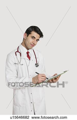 Stock Image - Portrait of an Indian male doctor writing prescription over light gray background. Fotosearch