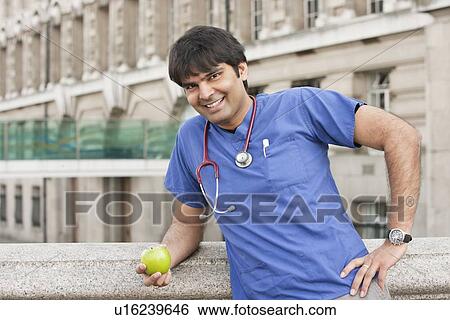 Stock Photograph - Portrait of an Indian male doctor holding a green apple. Fotosearch