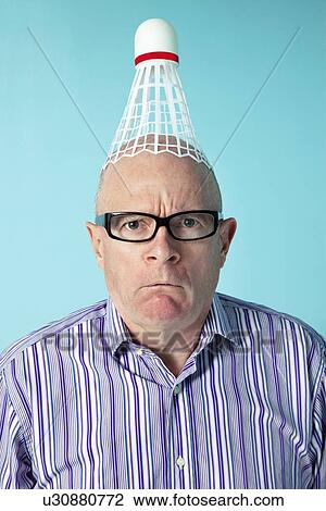 Stock Image - Portrait of angry man with shuttlecock on head over colored background. Fotosearch