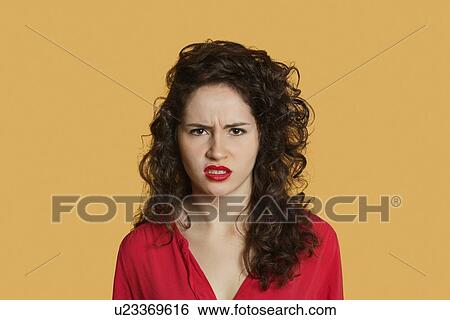 Stock Photograph - Portrait of angry young woman frowning over colored background. Fotosearch
