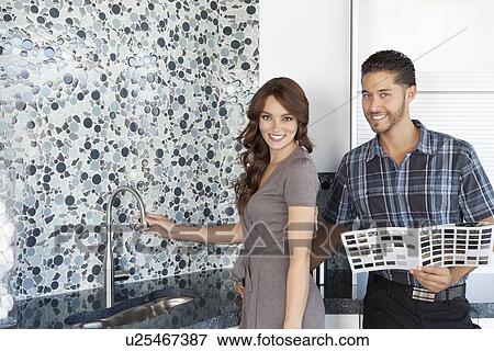 Stock Photo - Portrait of beautiful young couple with color samples standing in model home kitchen. Fotosearch