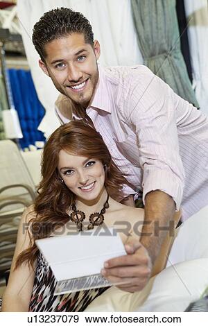 Stock Photo - Portrait of beautiful young woman sitting on chair with man in background. Fotosearch