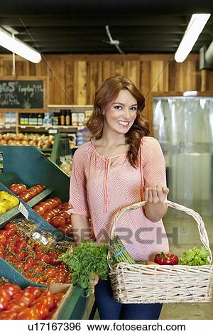 Portrait of beautiful young woman holding basket near tomato stall in market View Large Photo Image Stock Photograph - Portrait of beautiful young woman holding basket near tomato stall in market. Fotosearch