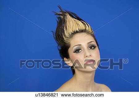 Stock Image - Portrait of beautiful young woman with spiked hair posing over blue background. Fotosearch