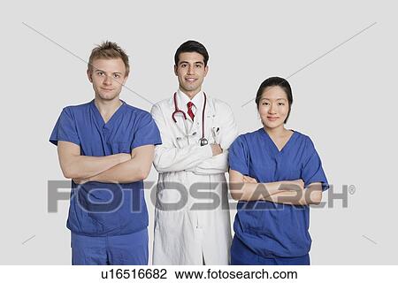 Stock Image - Portrait of diverse healthcare workers standing with hands folded over gray background. Fotosearch