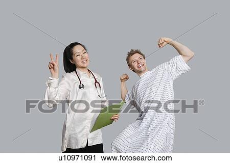 Stock Image - Portrait of doctor gesturing peace sign with patient cheering up. Fotosearch