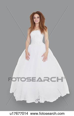 Portrait of elegant young brunette in wedding dress standing over gray background View Large Photo Image Picture - Portrait of elegant young brunette in wedding dress standing over gray background. Fotosearch