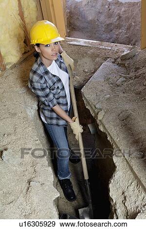Stock Photo - Portrait of female worker digging with shovel at construction site. Fotosearch