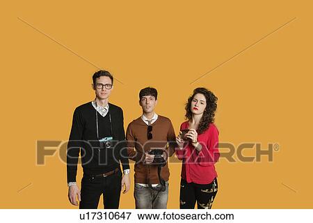 Stock Photo - Portrait of friends standing together with cameras over colored background. Fotosearch