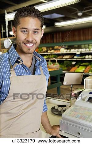 Portrait of handsome store employee standing near cash register in supermarket View Large Photo Image Stock Photo - Portrait of handsome store employee standing near cash register in supermarket. Fotosearch