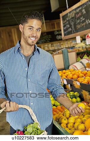 Stock Image - Portrait of handsome young man shopping for fruits in market. Fotosearch