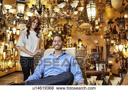 Stock Photo - Portrait of handsome young man sitting while woman standing background in lights store. Fotosearch