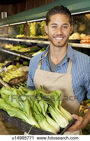 Stock Image - Portrait of handsome young sales clerk with bok choy in market. Fotosearch
